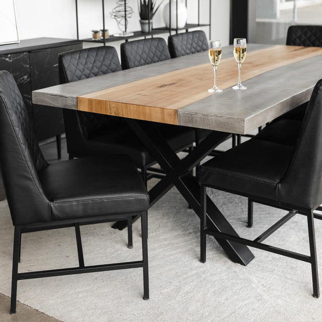 table de salle a manger industrielle avec plateau en bois et beton gris, pieds en metal noir et chaises en cuir noir capitonne.