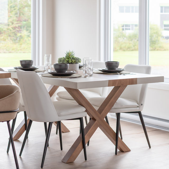 table de salle a manger moderne en bois et resine blanche avec pieds croises et chaises blanches a pieds noirs.
