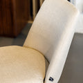 Chaise de salle à manger en tissu beige avec piètement noirs, placée près d’une table en bois dans un intérieur moderne.
