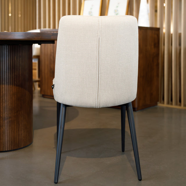 Chaise de salle à manger en tissu beige avec piètement noirs, placée près d’une table en bois dans un intérieur moderne.