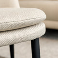 Chaise de salle à manger en tissu beige avec piètement noirs, placée près d’une table en bois dans un intérieur moderne.