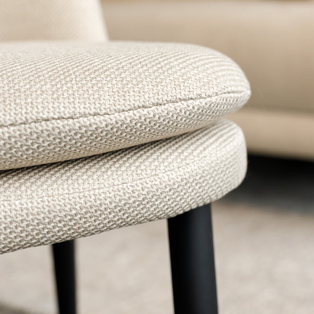 Chaise de salle à manger en tissu beige avec piètement noirs, placée près d’une table en bois dans un intérieur moderne.