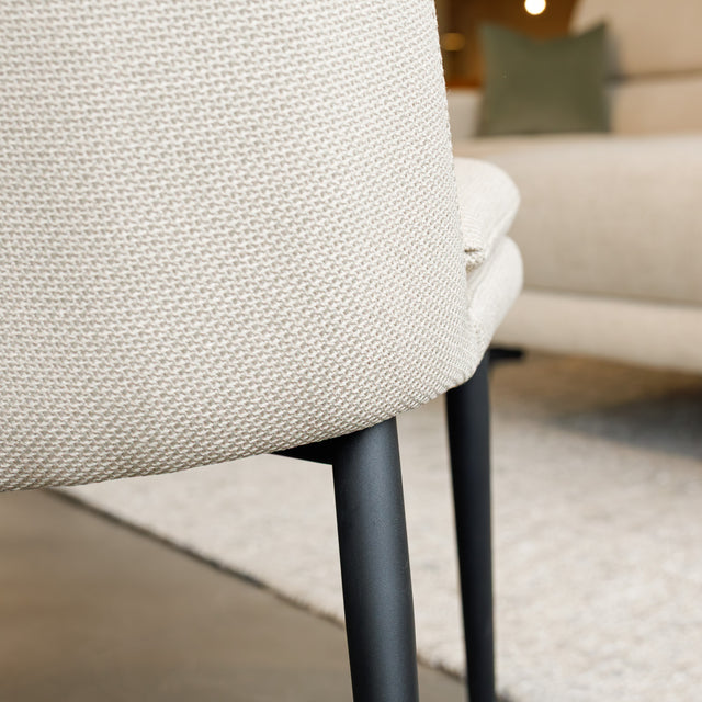 Chaise de salle à manger en tissu beige avec piètement noirs.