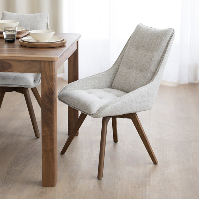 Chaise de salle à manger en tissu truffle sauvage avec piétement en bois noyer, placée près d’une table en bois moderne.