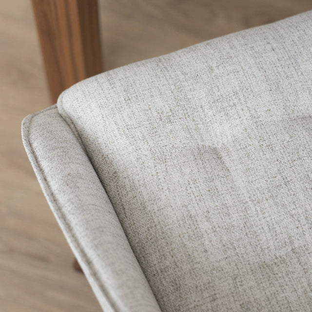 Chaise de salle à manger en tissu truffle sauvage avec piétement en bois noyer, placée près d’une table en bois moderne.