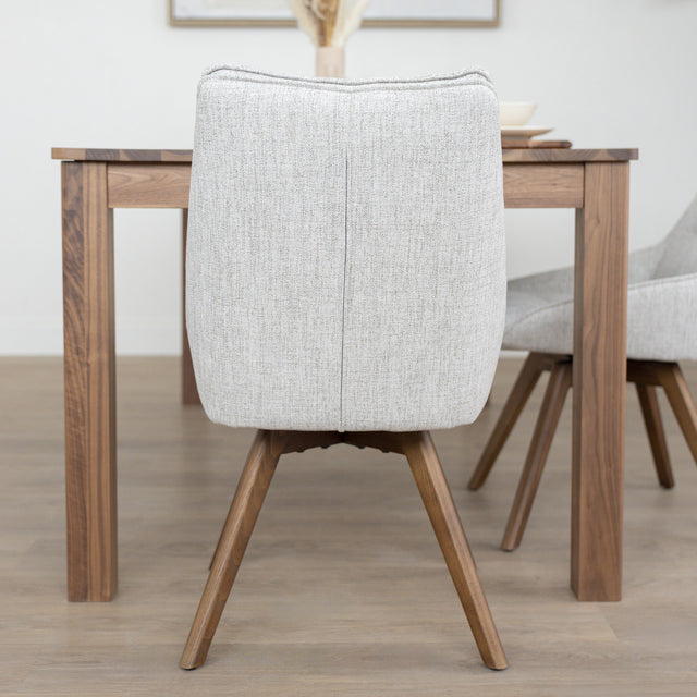 Chaise de salle à manger en tissu truffle sauvage avec piétement en bois noyer, placée près d’une table en bois moderne.