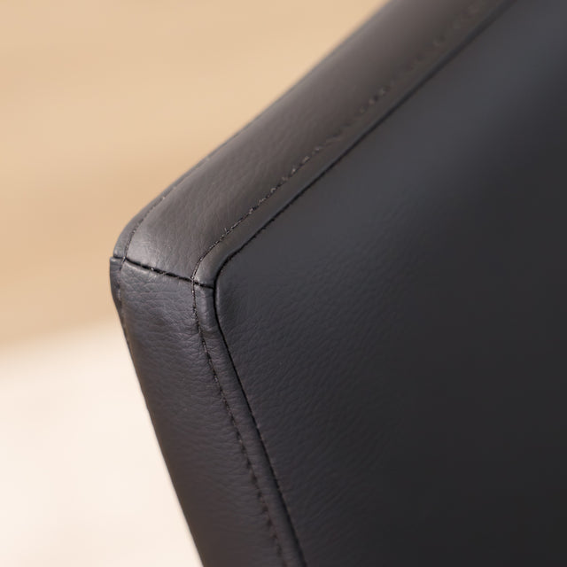 Chaise de cuisine en cuir végane noir  avec pieds assortis autour d’une table en bois moderne.
