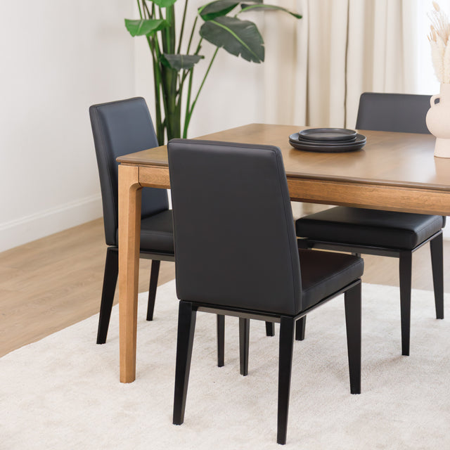 Chaise de cuisine en cuir végane noir  avec pieds assortis autour d’une table en bois moderne.