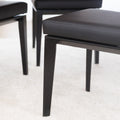 Chaise de cuisine en cuir végane noir  avec pieds assortis autour d’une table en bois moderne.