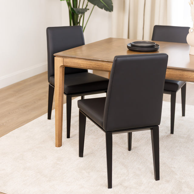 Chaise de cuisine en cuir végane noir  avec pieds assortis autour d’une table en bois moderne.