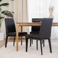 Chaise de cuisine en cuir végane noir  avec pieds assortis autour d’une table en bois moderne.