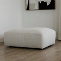 pouf rectangulaire beige clair en tissu sur sol en bois clair.
