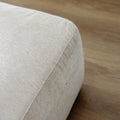 detail du bord inferieur d un pouf beige clair en tissu sur sol en bois.
