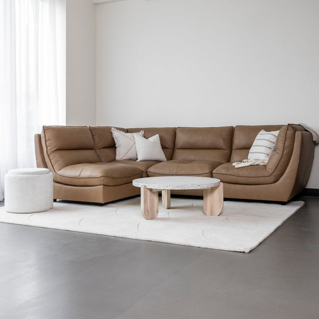 canape d angle en cuir brun clair avec coussins beiges sur tapis creme.