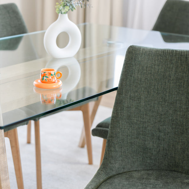 Chaise rembourrée en tissu vert avec dossier incurvé et pieds en bois, autour d’une table à manger au design moderne.