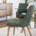 Chaise rembourrée en tissu vert avec dossier incurvé et pieds en bois, autour d’une table à manger au design moderne.