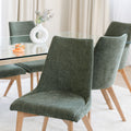 Chaise rembourrée en tissu vert avec dossier incurvé et pieds en bois, autour d’une table à manger au design moderne.