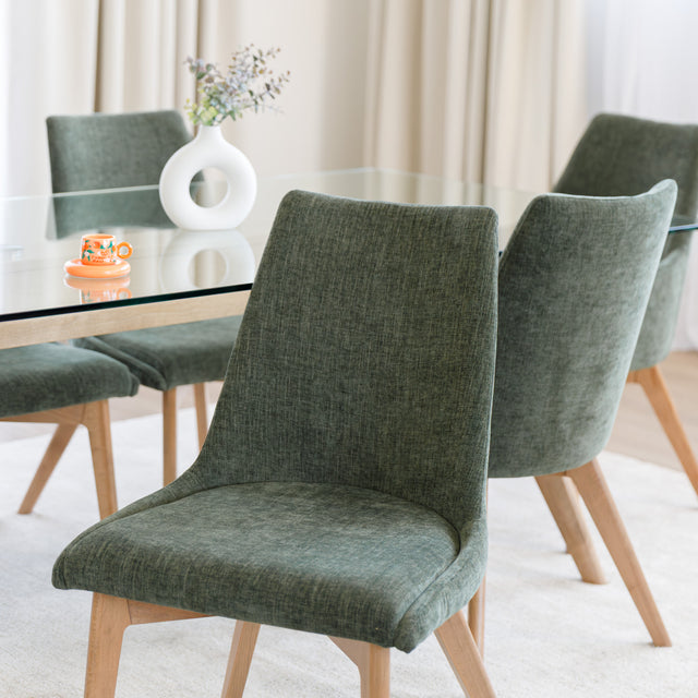 Chaise rembourrée en tissu vert avec dossier incurvé et pieds en bois, autour d’une table à manger au design moderne.