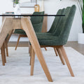 Chaise rembourrée en tissu vert avec dossier incurvé et pieds en bois, autour d’une table à manger au design moderne.