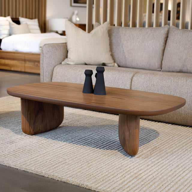Table basse ovale en bois noyer dans un salon moderne avec un canapé beige.