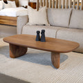 Table basse ovale en bois noyer dans un salon moderne avec un canapé beige.