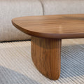 Table basse ovale en bois noyer dans un salon moderne avec un canapé beige.