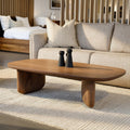 Table basse ovale en bois noyer dans un salon moderne avec un canapé beige.
