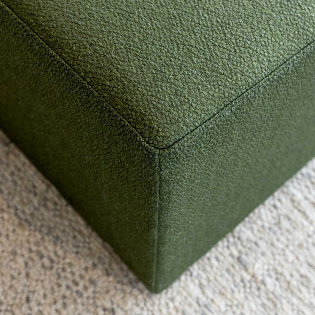 Détail ottoman carré vert en tissu texturé, finition soignée et angle net pour salon moderne.