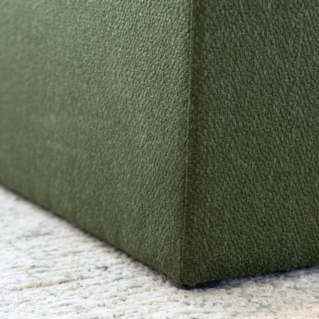 Détail ottoman carré vert en tissu texturé, finition soignée et angle net pour salon moderne.