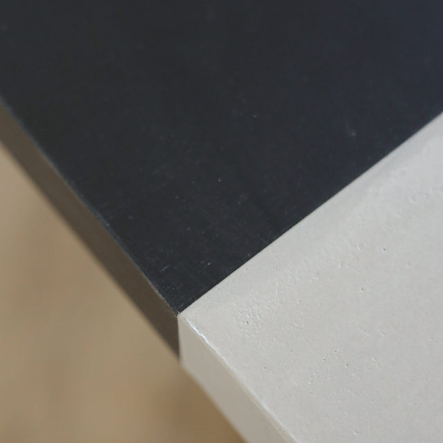 Table à manger moderne avec plateau béton ciment, tranche de frêne noir et piètement en métal noir, idéale pour salle à manger contemporaine.