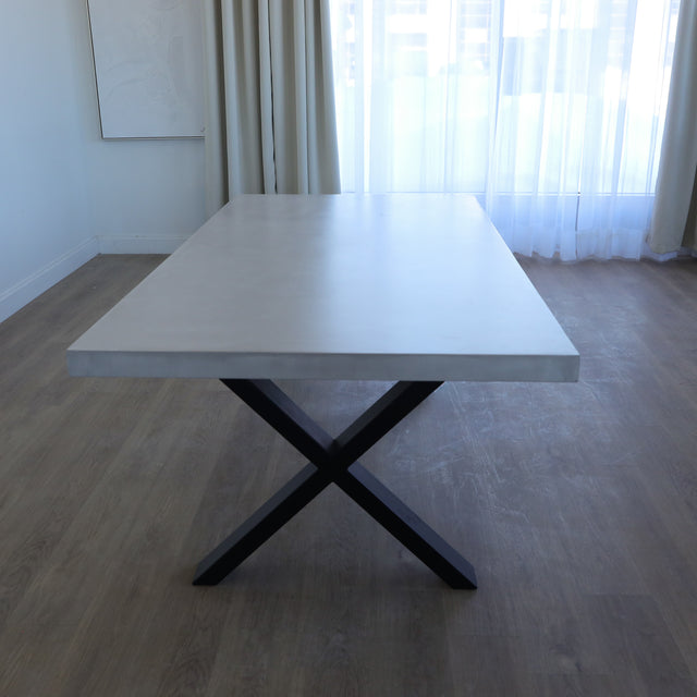 Table de salle à manger au design rectangulaire, plateau clair et piétement en X noirs, dans une salle à manger lumineuse.