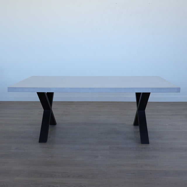 Table de salle à manger au design rectangulaire, plateau clair et piétement en X noirs, dans une salle à manger lumineuse.