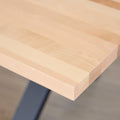 Image rapprochée d'une table rectangulaire en bois clair avec pieds en metal noir en X, design industriel elegant.