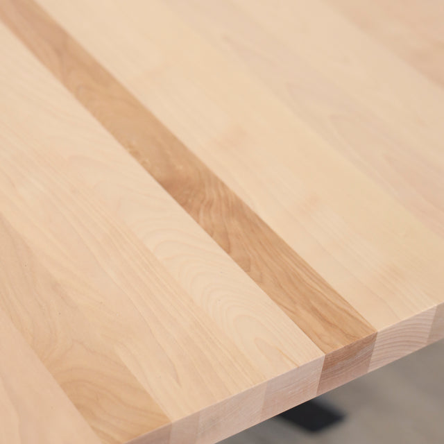 Image rapprochée d'une table rectangulaire en bois clair avec pieds en metal noir en X, design industriel elegant.