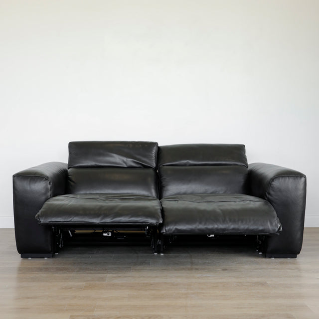 canape relax en cuir noir avec dossiers inclinables et repose pieds ouverts sur parquet clair.
