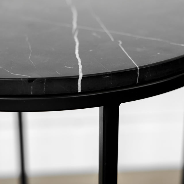Gros plan d’un plateau en marbre noir veiné de blanc, soulignant la finesse de ses motifs naturels et son bord arrondi au-dessus d’une structure métallique noire.
