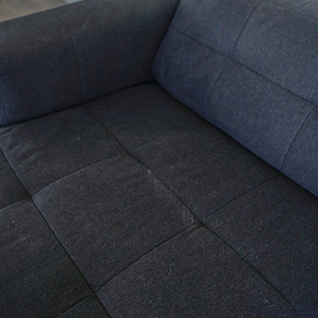 Detail de l assise du canape gris fonce en tissu matelasse au style moderne.
