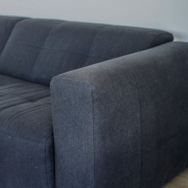 Detail de l accoudoir du canape gris fonce en tissu matelasse moderne.
