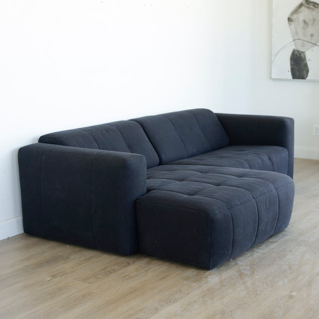 Canape d angle gris fonce matelasse au design moderne et lignes epurees.
