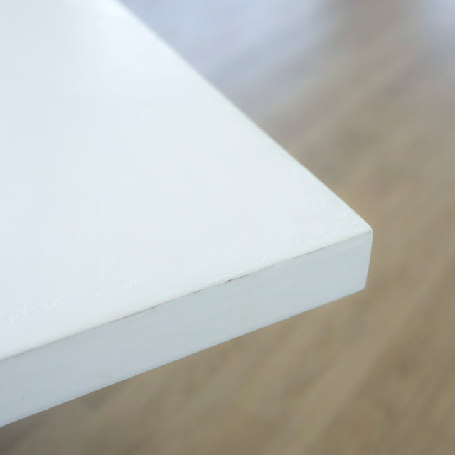 gros plan du bord d’un plateau de table blanc mat, montrant une finition lisse et angulaire sur fond de sol en bois clair.
