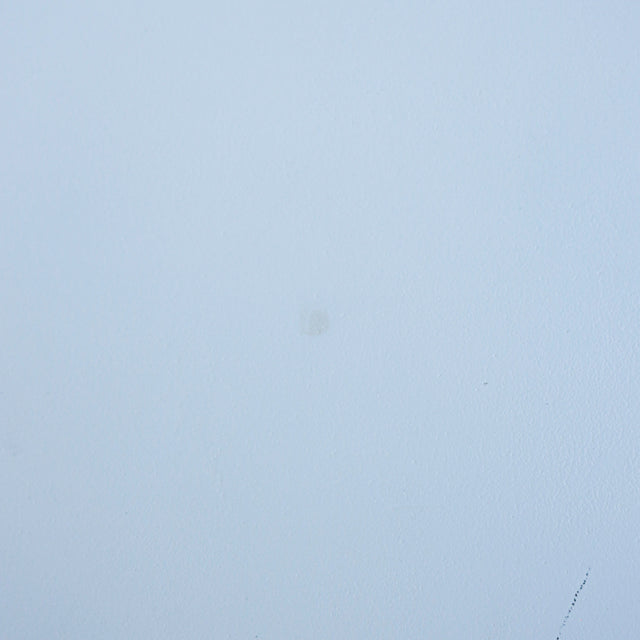 gros plan d’une surface blanche mate, présentant une légère marque circulaire au centre et une fine rayure en bas à droite.
