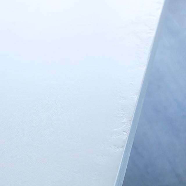 gros plan d’un coin de plateau de table blanc mat, montrant une texture lisse avec des irrégularités légères le long du bord.
