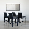 ensemble de tabourets comptoir en cuir végane noir avec coutures blanches et pieds en bois sombre.
