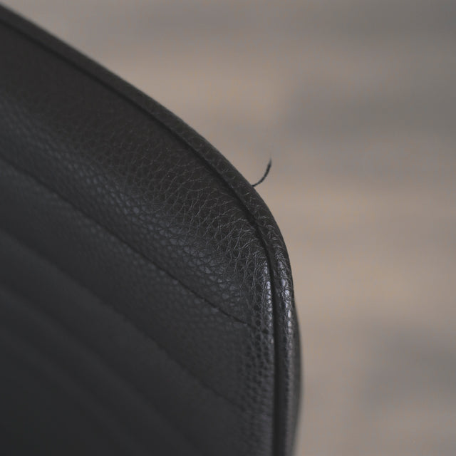 image rapprochée d'un ensemble de chaises moderne en simili cuir noir avec dossier a coutures horizontales et pieds en metal. Comportant un fil tiré.