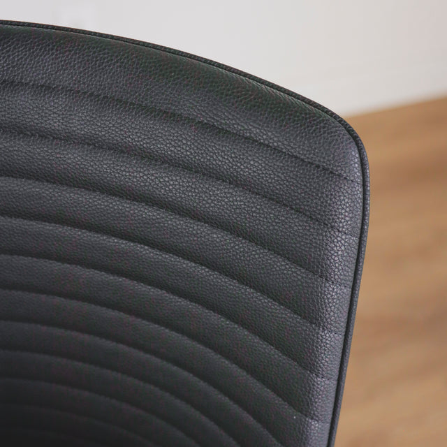 image rapprochée d'une chaise moderne en simili cuir noir avec dossier a coutures horizontales et pieds en metal.
