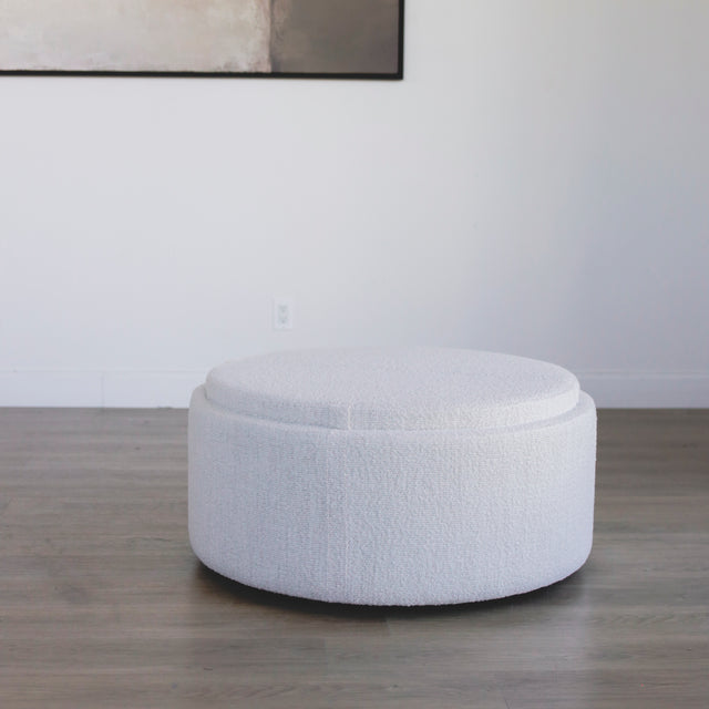 ottoman rond en tissu blanc bouclé avec plateau en bois amovible sur sol en bois.