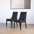 Ensemble de chaises moderne en cuir noir avec coutures blanches et pieds en bois sombre.
