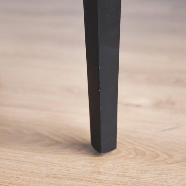 image rapprochée d'une patte d'un ensemble de chaises moderne en cuir noir avec coutures blanches et pieds en bois sombre.