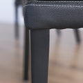 image rapprochée d'un ensemble de chaises moderne en cuir noir avec coutures blanches et pieds en bois sombre.