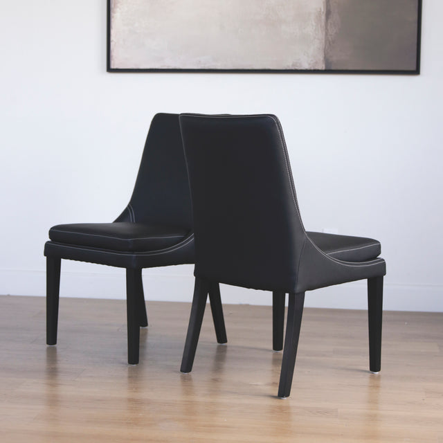 Ensemble de chaises moderne en cuir noir avec coutures blanches et pieds en bois sombre.